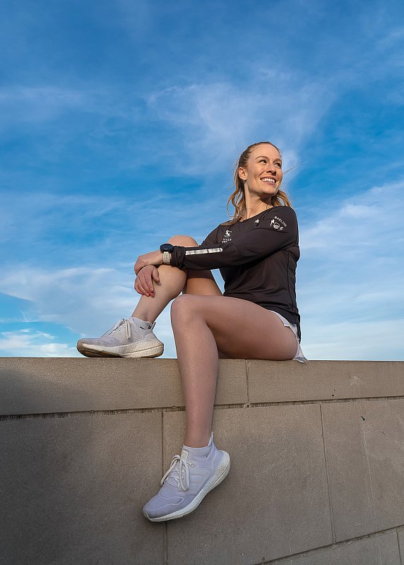 Woman entrepreneur and running coach sitting on a concrete barrier outside with blue sky
